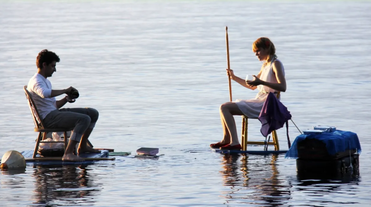 Two artists seated on platforms while working on a lake