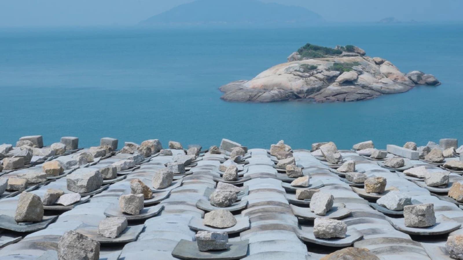 Stone-weighted tile roofs overlooking the sea and a small rocky island in the Matsu Islands
